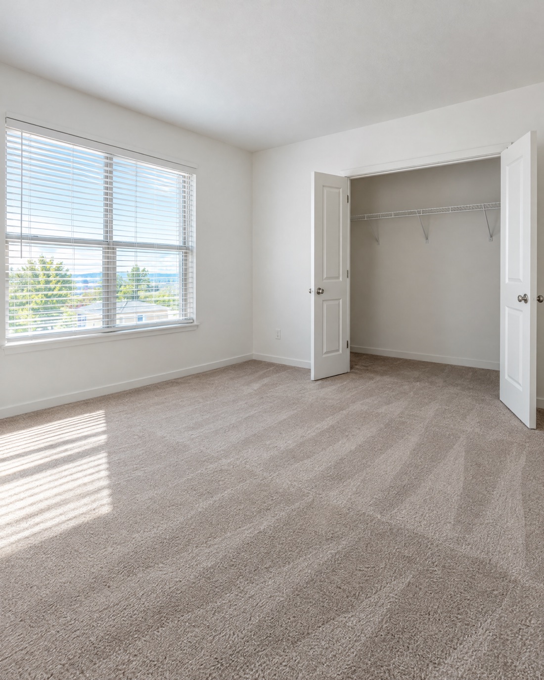 A bright, empty bedroom with fresh vacuum lines in the carpet